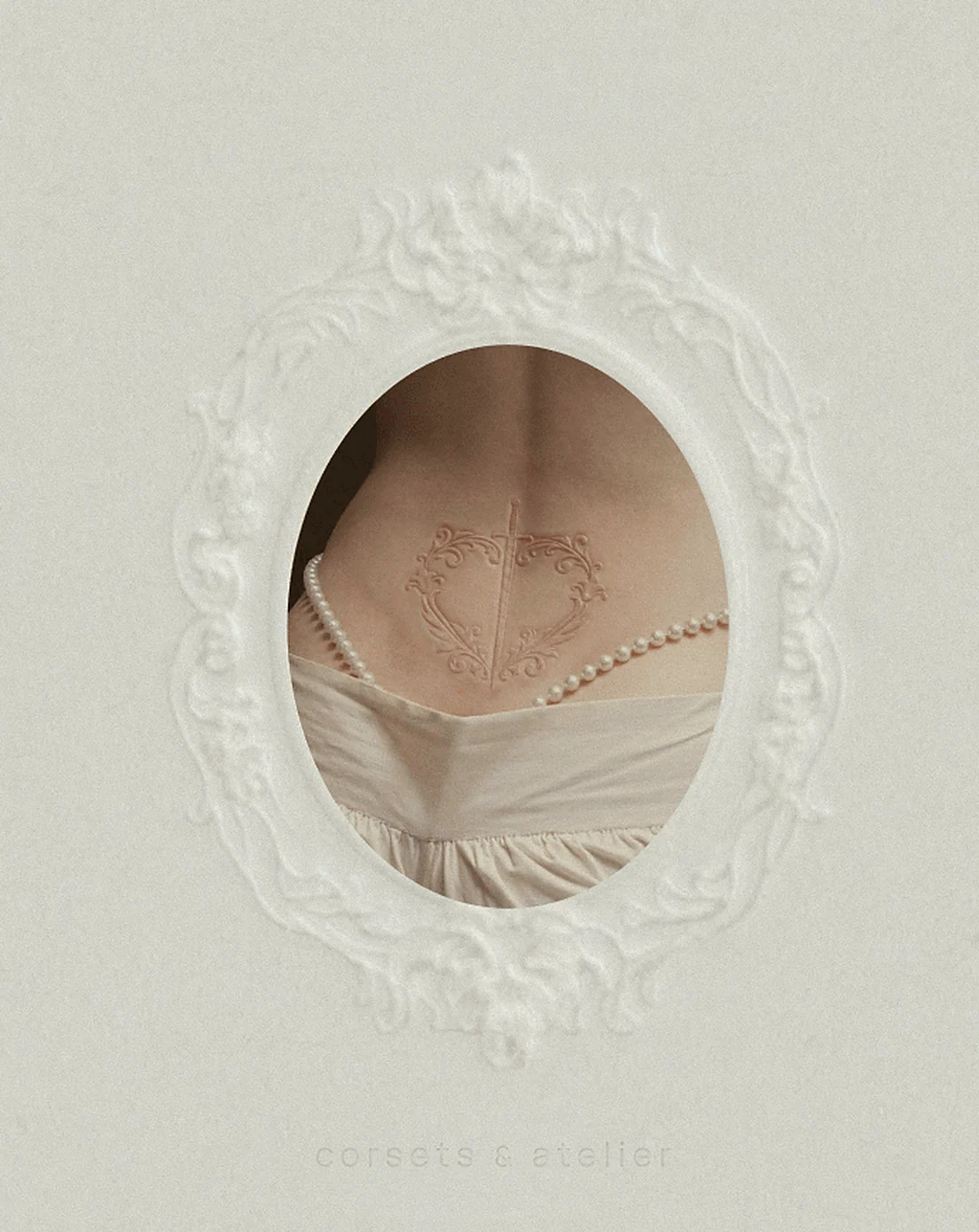 An embossed oval frame on ivory paper revealing a bare back with the KUG crest pressed into the skin above a pearl necklace